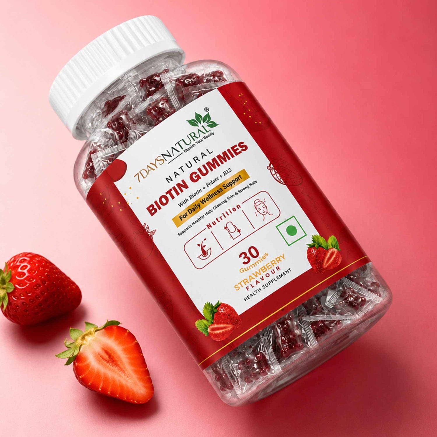 A bottle of Days Natural Biotin Gummies, strawberry flavor, shown at an angle on a pink background with fresh strawberry slices as props.